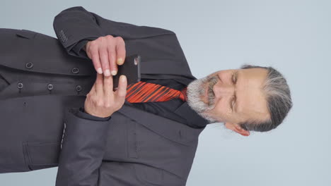 Vertical-video-of-Old-businessman-texting-on-the-phone.-Happy-emoticon.